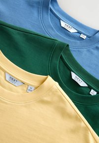 Trois t-shirts à col rond pliés en bleu, vert et jaune, chacun avec des étiquettes de taille "NEXT Relaxed Fit" visibles.