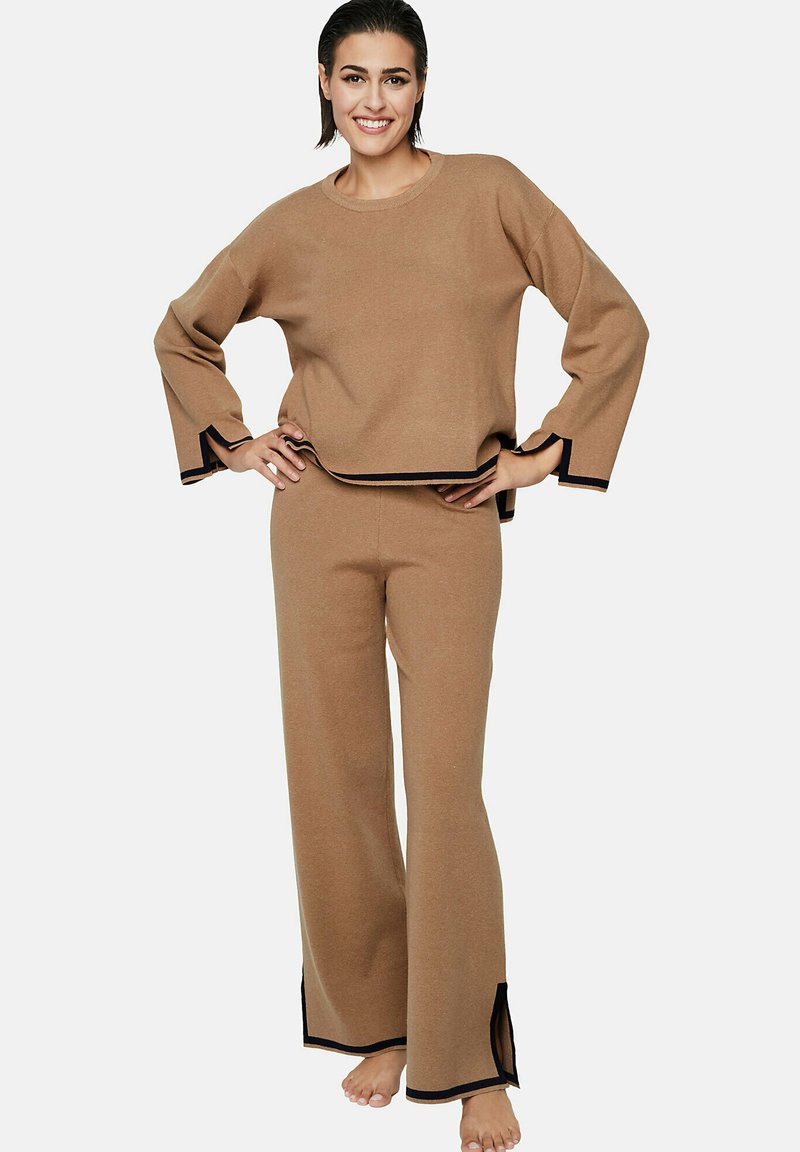 Tweedelig loungewear-set in tan, gemaakt van een textuurstof. Het topje heeft wijde mouwen met zwarte accenten; de broek is flair met zijsplits.
