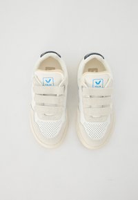 Valged tennisekad beeži nahkjätkumisega, millel on perforatsiooni kaudu sõrmeosa, kolm Velcro rihma ja sinine logotagi keele peal.