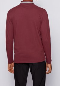 Långärmad, mörkröd polo-tröja i mjukt tyg. Har en krage med kontrasterande ränder. Sömmar detaljer och en avslappnad passform.