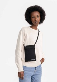 Zwarte textielen schoudertas met een textuurafwerking, voorzien van een voorkantvak, zilveren hardware, en een verstelbare strap met stippen.