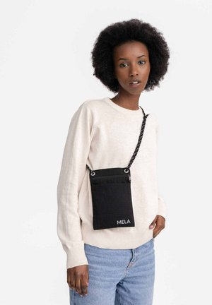 Sac bandoulière noir en textile avec une finition texturée, comportant une poche avant, du matériel argenté et une sangle réglable à pois.