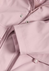 Růžová voděodolná bunda s hladkou texturou a zipovým uzávěrem. Má patentky a žebrované manžety pro větší pohodlí.