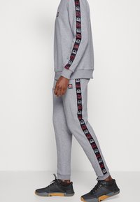 Grijze sportoutfit met logo-accenten op de mouwen en broek. Materiaal is zacht met een gladde textuur. In combinatie met zwarte sportschoenen.