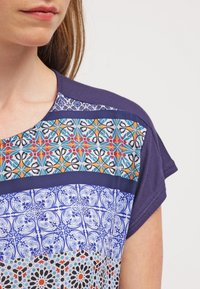 Korte ærmede top med en marineblå sektion og flere intrikate mønstre i blå, orange og sort, med varierende teksturer og designs.