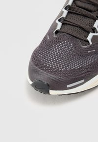 Chaussure de course pour homme avec une tige en mesh gris foncé, des accents blancs, une semelle noire, des détails réfléchissants et un embout texturé.