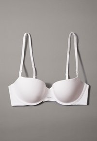 Sostén de tela suave blanca con copas acolchadas y tirantes ajustables. Cuenta con un cierre lateral y una pequeña etiqueta que muestra "Calvin Klein."
