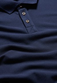 Námornícky polos tričko s textúrovanou látkou, tromi hnedými gombíkmi a klasickým golierom. Hladký, preložený materiál je viditeľný.