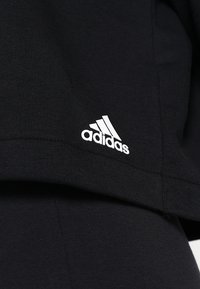 Sweatshirt noir en coton à manches courtes, avec un logo Adidas blanc sur le côté gauche. Texture lisse et design décontracté.