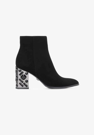 Stivaletto in suede nero con punta affusolata e tacco geometrico in blocco di metallo argentato con accenti neri e texture.