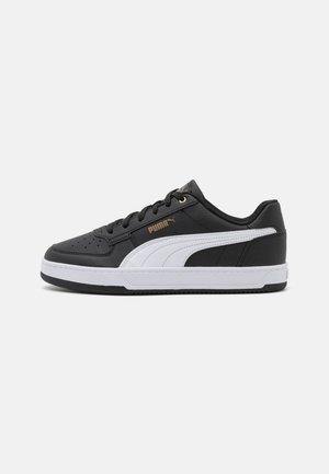 Sneaker sportive nere con accenti bianchi, texture simile alla pelle, punta tonda, design con allacciatura e dettaglio del logo dorato sul lato.
