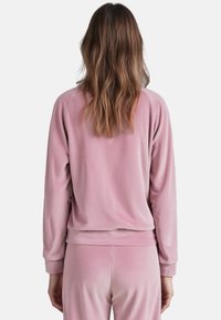 Pullover lungo a maniche corte di un delicato colore rosa, realizzato in un tessuto morbido; presenta un collo rotondo e una vestibilità comoda. Vista dal retro con maniche con polsini.