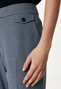 Pantaloni a motivo houndstooth bianco e nero con bottone nero e tasca laterale, caratterizzati da un tessuto strutturato e una vestibilità sartoriale in vita.