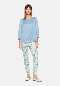 Light blue satin blouse with a round neckline and puffed sleeves, paired with patterned slim-fit pants in green and cream, and white flats.