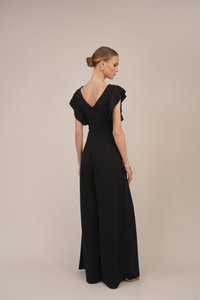 Tuta nera con maniche a sbuffo, design con scollatura a V sul retro, corpino strutturato, gambe larghe, tessuto liscio e dettaglio di bottone discreto sul retro.