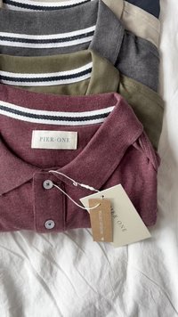 Quattro polo shirt impilati, nei colori bordeaux, verde oliva, grigio e crema. Ognuno ha un colletto a righe e le etichette visibili.