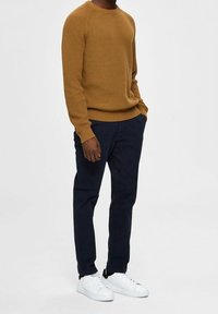 Hořčicový žebrovaný svetr, tmavě modré zúžené kalhoty a bílé tenisky. Texturovaný úplet, kulatý výstřih a minimalistický design pro volný čas.