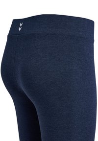 Nahaufnahme dunkelblauer enganliegender Leggings mit hohem Bund und kleinem weißem Doppelwinkel-Logo am hinteren Bund.