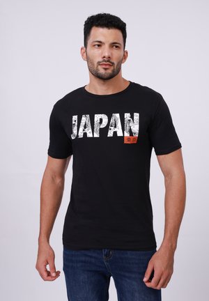 Sort bomulds t-shirt med fed hvid "JAPAN" tekst med intrikate mønstre og et lille rødt rektangel med japanske tegn.