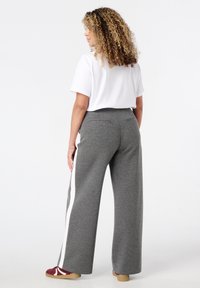 Grijze wijde broek met witte zijstrepen, elastische tailleband en twee achterzakken, gecombineerd met een eenvoudig wit T-shirt en casual schoenen.