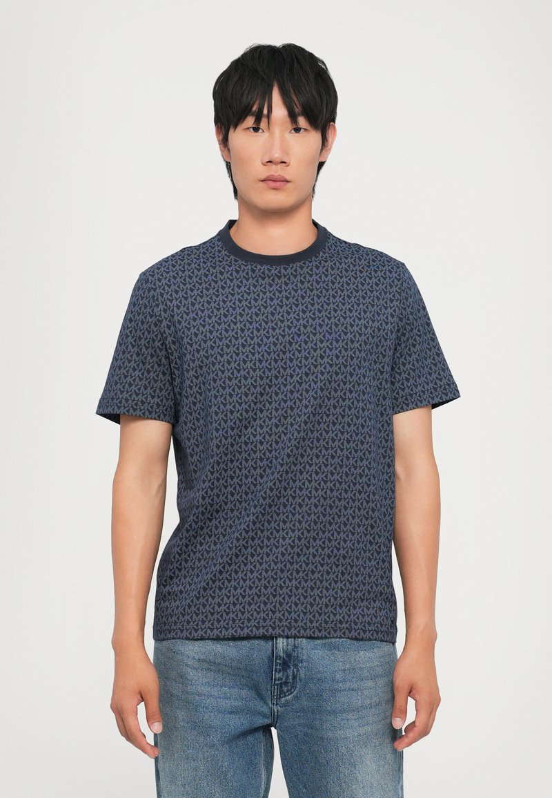 Tricou scurt, de culoare albastru marin, cu un model geometric repetat, guler rotund și material moale. Asortat cu blugi de culoare bleu deschis.