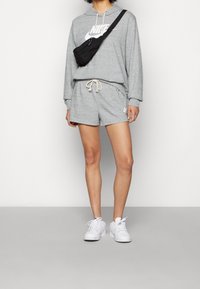 Ljusgrå Nike-hoodie med stor logotyp, tillsammans med matchande shorts och vita sneakers. Inkluderar en svart axelremsväska.