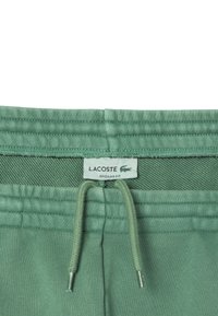 Jogging en coton vert avec une ceinture texturée, équipée d'un cordon de serrage et d'une petite étiquette "Lacoste". Design à coupe régulière.
