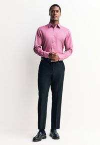 Różowa koszula z długim rękawem z kołnierzykiem na guziki, w połączeniu z czarnymi spodniami i błyszczącymi czarnymi butami. Gładka tkanina, dopasowany krój.
