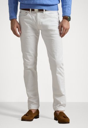 Jeans de denim blanco de corte slim, combinados con un suéter de punto de cable azul claro y mocasines de ante marrones. Los detalles incluyen un cinturón y un reloj.