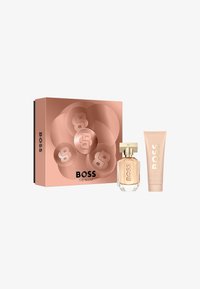 Conjunto de regalo BOSS The Scent que incluye una botella de perfume de cristal transparente con acentos dorados, un tubo de crema rosa y una caja en color oro rosa con diseño de logo.