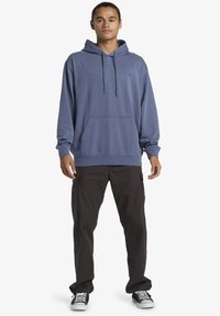 Blue hoodie with a front pocket, drawstring hood, and logo detail. Paired with dark cargo pants and black shoes. Simple, casual design.