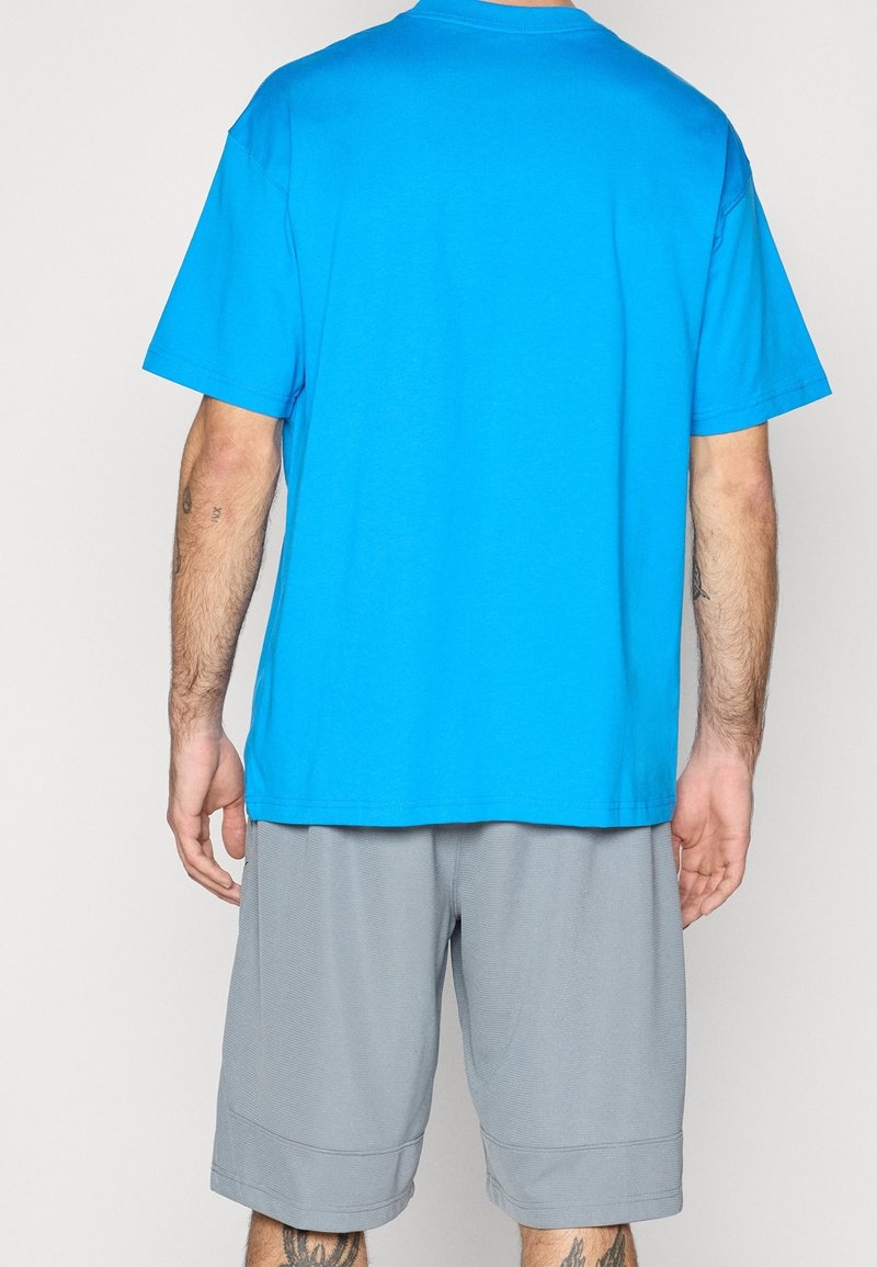 T-shirt en coton bleu à manches courtes, col rond et coupe décontractée, associé à un short de sport gris avec un tissu texturé et une taille élastique.
