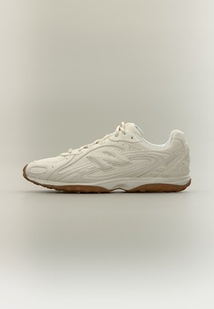 Scarpa sportiva color bianco sporco con suola marrone, taglio basso, design con lacci e motivi strutturati lungo i lati e il tallone.