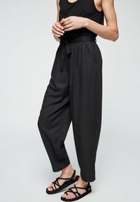 Pantalons noirs taille haute avec une coupe décontractée et des poches latérales, fabriqués en tissu lisse. Une ceinture assortie souligne la taille.