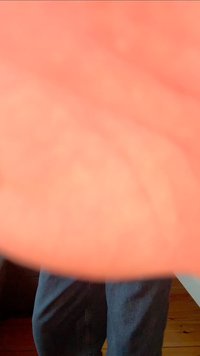 Un primo piano di una mano parzialmente offuscata, che mostra una superficie della pelle liscia e di un rosa chiaro con una forma curvilinea, contro uno sfondo sfocato.