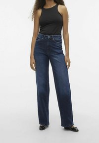 Höga mörka denimjeans med vida ben, med en klassisk femfickdesign och en slät, jämn textur. Kombineras med en figurnära svart linne.