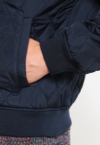 Chaqueta acolchada de navy con puños y cintura de canalé. Presenta bolsillo lateral, textura suave y diseño acolchado para el aislamiento.