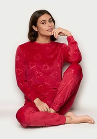 Sæt med rød fløjl pyjamas, der inkluderer en langærmet top og bukser med hjerte mønster. Blød tekstur og tætsiddende design, velegnet som loungewear.