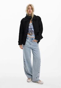 Černá péřová bunda, krátké modré tričko s potiskem, světle modré džíny širokých nohavic s bočními knoflíky a béžové nazouvací boty.