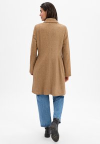 Brown herringbone coat with a single-breasted design, notched collar, and long sleeves, paired with high-waisted blue jeans and black boots.