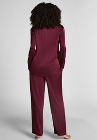Ensemble de loungewear bordeaux comprenant un haut à manches longues et un pantalon assorti, avec une texture lisse, des rayures verticales et une coupe décontractée.