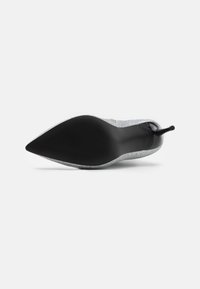 Zapato de tacón alto de punta afilada con parte superior de tela con brillo plateado y suela negra lisa, que presenta un tacón de aguja delgada para mayor soporte.