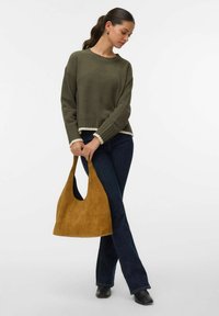 Suéter de punto verde oliva con ribete crema, combinado con jeans oscuros y un bolso de ante marrón claro. Botines negros completan el look.