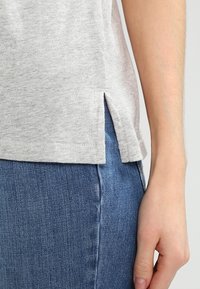 Maglietta grigia in cotone con spacchi laterali all'orlo e vestibilità casual. Abbinata a jeans di denim blu per contrasto.