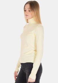 Maglione dolcevita color crema realizzato in tessuto morbido, design aderente, maniche lunghe con polsini a coste e orlo dritto.