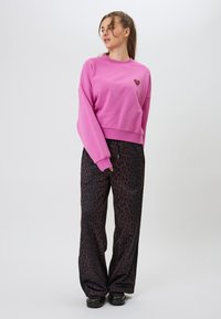 Vaaleanpunainen lyhythihainen collegepusero, jossa on sydänlogo rinnan kohdalla, yhdistettynä mustiin leopardi-neliöhousuihin. Sileä kangas, rento istuvuus.