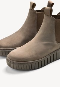 Bottines Chelsea en suède marron avec des panneaux élastiques sur les côtés et une semelle en caoutchouc texturée. Elles disposent d'un bout arrondi et de languettes pour un enfilage facile.