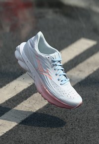Lettvekt atletisk sko med hvit overdel, rosa detaljer og blå snørebånd. Har ventilasjonsåpninger og en polstret såle for komfort.
