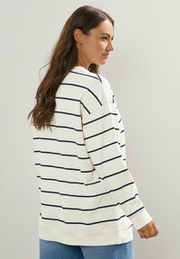 Randig sweatshirt i krämfärgad med marinblå linjer, med avslappnad passform, lång ärm och ribbade manschetter. Mjuk tyg med en slät textur.