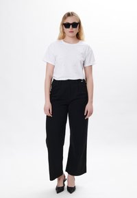 Camiseta de algodón blanca con adornos combinada con pantalones de tiro alto de pierna ancha negros y tacones negros de punta.